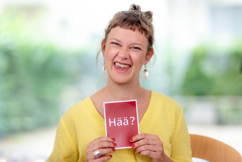 Inga hält eine Karte in der Hand, auf der "Hää?" steht.